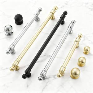 May include: A collection of cabinet hardware, including silver, gold, and black handles and knobs. The handles are bar-style with ball-shaped ends. The knobs are round and come in silver, gold, and black finishes. The hardware is displayed on a white marble surface.