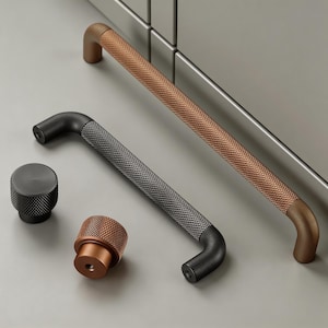 May include: A collection of cabinet hardware, including two bar pulls and two knobs. The bar pulls have a textured, diamond pattern in copper and dark gray. The knobs are copper and dark gray, with a similar textured pattern.
