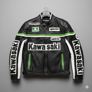 Op de afbeelding: Zwarte leren motorjas met witte en groene accenten. Voorzien van het Kawasaki-logo op de voorkant en mouwen, samen met patches van Michelin en Alpinestars. De jas hangt aan een zwarte hanger.