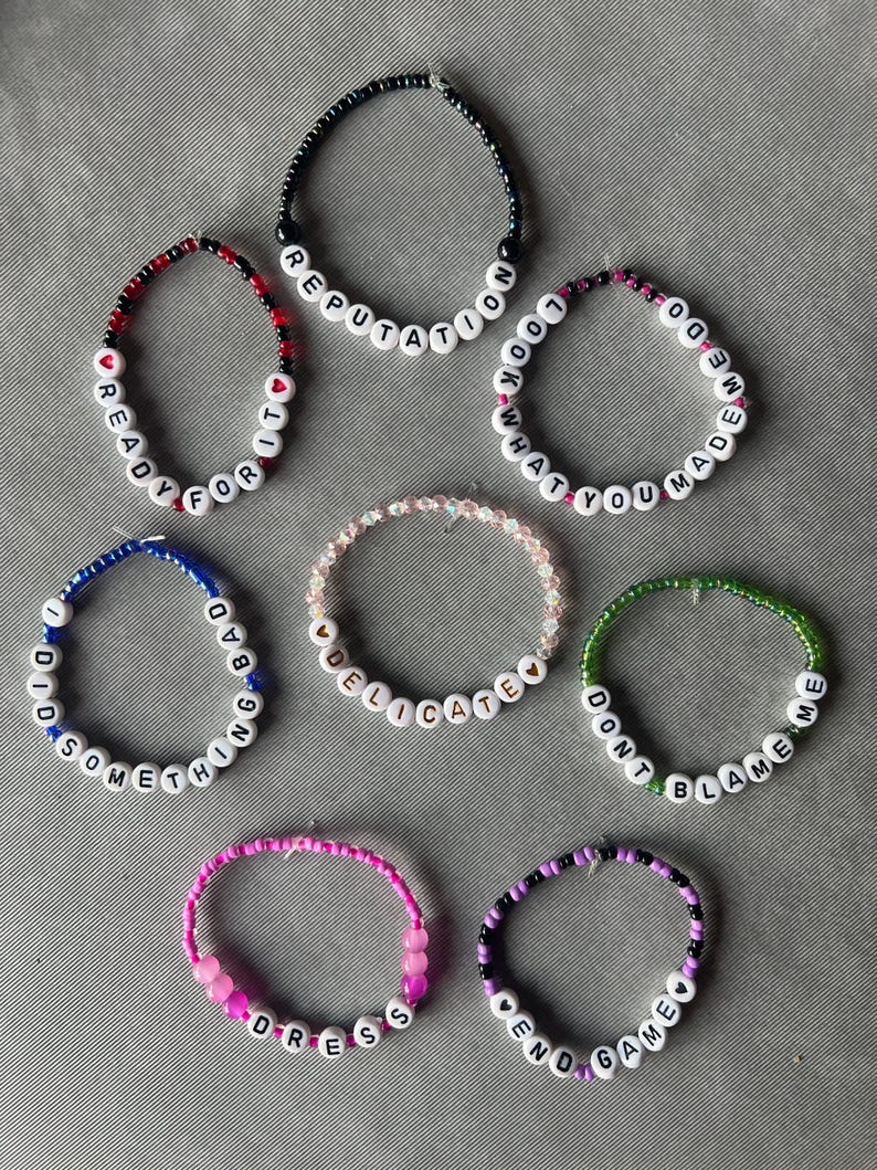 May include: Seven beaded bracelets featuring white letter beads spelling out REPUTATION, READY FOR IT, LOOK WHAT YOU MADE ME DO, I DID SOMETHING BAD, DELICATE, DONT BLAME ME, DRESS, and END GAME, accented with various colored beads and small heart shapes.