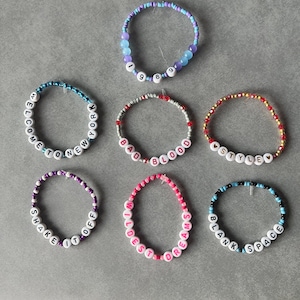 May include: Seven circular beaded bracelets featuring colorful plastic beads and white letter beads. The bracelets display text including 1989, Welcome to New York, Bad Blood, Style, Shake It Off, Wildest Dreams, and Blank Space with heart accents.