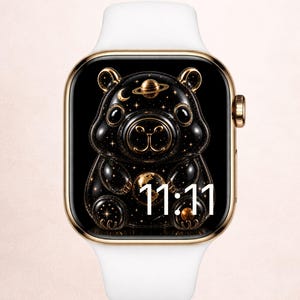 May include: A smartwatch with a gold-toned rectangular case and a white silicone band. The digital display features a black background with a glossy, stylized bear illustration decorated with gold stars, a planet, and the white digital time 11:11.