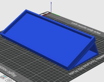 May include: A bright blue, rectangular tray with angled sides, likely 3D printed. The tray sits on a black and gray grid surface, possibly a printer bed. The design is simple and geometric.