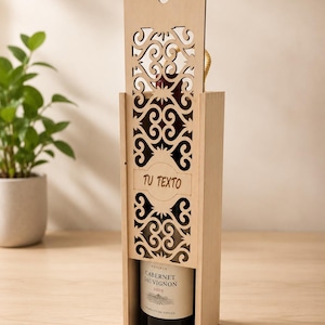 Może przedstawiać: Jasna drewniana skrzynka na butelkę wina z misternym ażurowym wzorem. Skrzynka mieści butelkę Cabernet Sauvignon 2020. Widoczny jest napis "TU TEXTO".