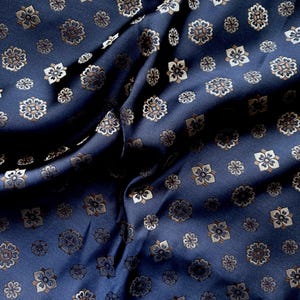 May include: Navy blue fabric with a repeating floral pattern in shades of brown and cream. The fabric is draped, creating shadows and highlights that emphasize the texture and design. This textile is suitable for apparel or home decor.