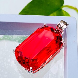 May include: A rectangular, faceted red gemstone pendant set in a silver-toned metal prong setting. The vibrant red stone features sharp, clean edges and a polished surface, with a silver bail attached to the top for hanging on a chain or cord.