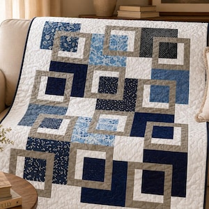 Pode incluir: Uma colcha com um padrão geométrico de quadrados entrelaçados em tons de azul-marinho, azul-claro, branco e cinzento. O tecido apresenta vários estampados florais e de pontos, com um fundo branco e um acabamento de borda azul-marinho.