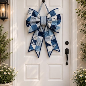 May include: A large decorative bow made of quilted fabric featuring a patchwork design in various shades of blue and white. The pattern includes nautical motifs like sailboats, stripes, and floral prints, with a central band of light blue fabric.