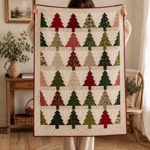 May include: A rectangular quilt featuring a repeating pattern of Christmas tree shapes in various shades of red, green, and neutral tones. The trees are arranged in rows against a light beige background, finished with a thin red fabric border.