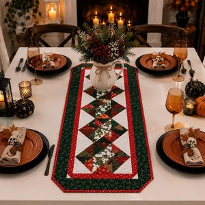 May include: A rectangular quilted table runner featuring a central pattern of green, red, and white geometric shapes with a dark green border. The runner is placed on a white table set with orange plates, black plates, wine glasses, and skull napkin rings.