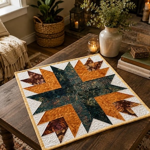 Pode incluir: Um centro de mesa acolchoado quadrado com um padrão de estrela central em tons de azul-petróleo escuro, laranja queimado e castanho com detalhes em branco. O tecido apresenta uma aparência texturizada e manchada com costuras intrincadas.