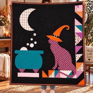 May include: A black quilt featuring a pink and black buffalo check cat wearing an orange witch hat, a teal cauldron with white bubbles, and a white plaid crescent moon. The border consists of orange diamonds and a vertical strip of colorful triangles.
