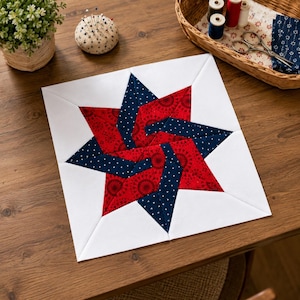 May include: A square quilt block featuring a central star design composed of red fabric with a circular pattern and dark blue fabric with a white dot pattern, all set against a white background with white corner triangles.