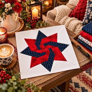 May include: A square fabric quilt block featuring a central star design. The star is composed of red fabric with a circular pattern and dark blue fabric with white polka dots, all set against a plain white background border.