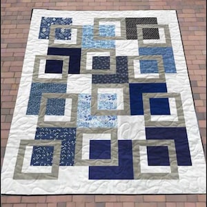 May include: A rectangular quilt featuring a geometric pattern of overlapping squares in shades of navy blue, light blue, and grey. The design incorporates various floral and polka dot prints on a white background with visible swirling stitch patterns.