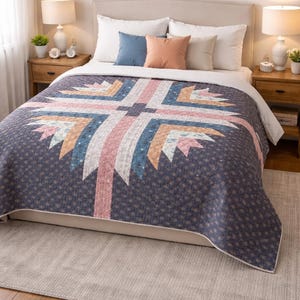 May include: A navy blue quilt with a geometric design in shades of pink, blue, and white. The quilt is on a bed with white bedding and decorative pillows. Two wooden nightstands with lamps flank the bed.