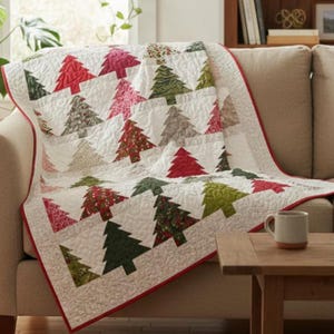 May include: A white quilt with a red border featuring a repeating pattern of Christmas trees in various colors and patterns. The quilt is draped over a beige sofa, creating a cozy, festive atmosphere.