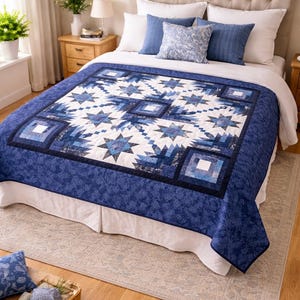 May include: A blue and white quilt with a star and geometric pattern covers a bed. The quilt features various shades of blue and white, with a dark blue border. Decorative pillows in shades of blue complete the bedding ensemble.