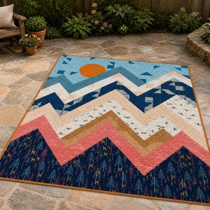 May include: A colorful quilt with a mountain range design. The quilt features a blue sky with an orange sun, and layers of mountains in shades of blue, pink, and brown. The bottom layer has a forest pattern.