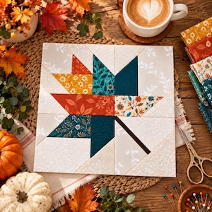 Op de afbeelding: Een vierkant quiltblok met een centraal esdoornbladontwerp opgebouwd uit diverse stoffen lapjes. Het blad toont bloemmotieven in oranje, petrol en mosterdgeel tegen een lichtcrème achtergrond met witte bladmotieven.