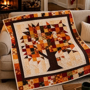 May include: A quilt featuring a central tree design composed of small squares in shades of orange, red, yellow, and brown. The tree has a solid dark brown trunk and is framed by a dark brown border and an outer edge of autumn leaf patterns.