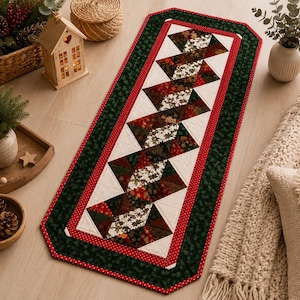 May include: A rectangular quilted table runner featuring a central geometric pattern of alternating dark green, deep red, and cream-colored fabric triangles. The runner is bordered by a thin red dotted line and a wide dark green fabric edge.