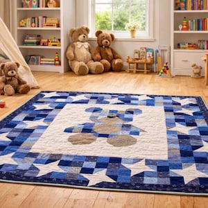 May include: A blue and white quilt with a teddy bear design in the center. The quilt features a border of white stars and blue squares. The quilt is on a hardwood floor in a child's room.