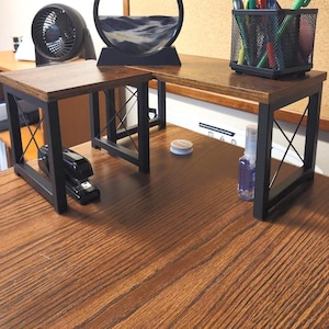 May include: A brown wooden desk with black metal legs. A black stapler sits on the desk. A black mesh pen holder, a small fan, and a sand art piece are also visible.