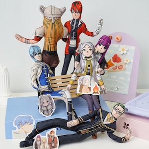 May include: A group of anime-style plush dolls with distinct character designs and clothing. The dolls are arranged on a bench and around a decorative display, featuring a variety of colours and patterns.