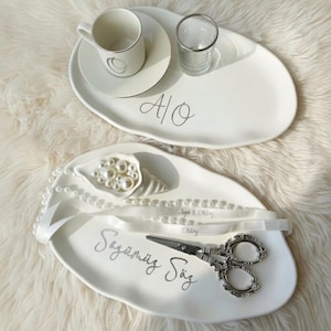 May include: Two white oval serving trays with silver accents. One tray has a cup and saucer, a small glass, and the letters "A/O". The other tray has a pearl bouquet, scissors, and the text "Sözümüz Söz".