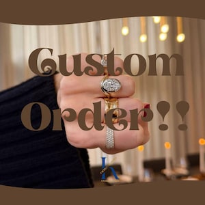 May include: A hand adorned with multiple rings, including a diamond cluster and gold bands. The image features the text "Custom Order!!" in a brown, decorative font. The background is blurred, with warm lighting.