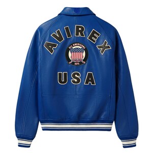 May include: A bright blue leather jacket featuring a ribbed collar, cuffs, and hem with white stripes. The back displays the text AVIREX in an arc, a circular patch with an American flag design and the text ALL AMERICANS ESTABLISHED 1975, and USA.
