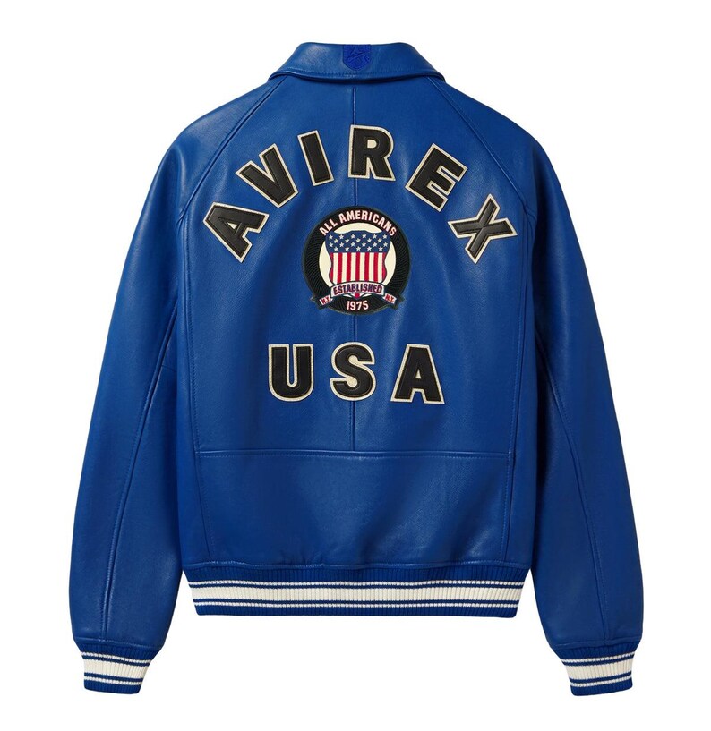 May include: A bright blue leather jacket featuring a ribbed collar, cuffs, and hem with white stripes. The back displays the text AVIREX in an arc, a circular patch with an American flag design and the text ALL AMERICANS ESTABLISHED 1975, and USA.