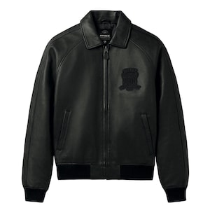 Puede incluir: Una chaqueta de cuero negro con cuello cl&aacute;sico, cremallera frontal completa y pu&ntilde;os y dobladillo acanalados. El pecho muestra un parche bordado en negro con el texto AVIREX. La chaqueta incluye dos bolsillos laterales verticales.