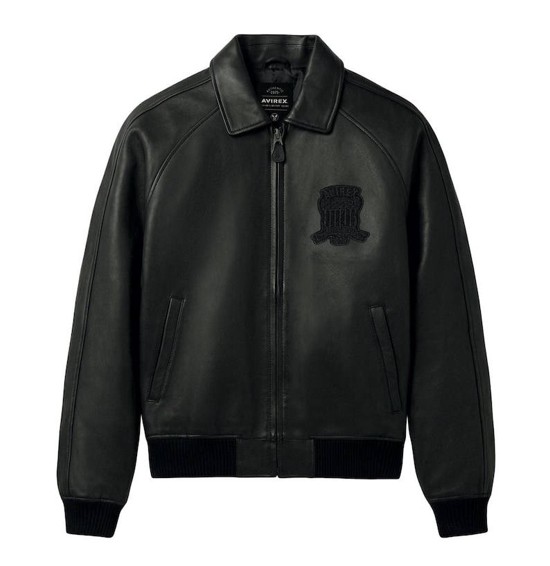Puede incluir: Una chaqueta de cuero negro con cuello cl&aacute;sico, cremallera frontal completa y pu&ntilde;os y dobladillo acanalados. El pecho muestra un parche bordado en negro con el texto AVIREX. La chaqueta incluye dos bolsillos laterales verticales.