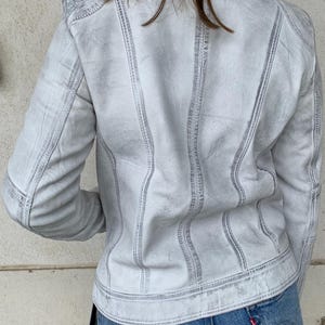 K&ouml;nnte beinhalten: Hellgraue Jeansjacke mit sichtbaren N&auml;hten. Die Jacke hat ein klassisches Design mit Kragen, Kn&ouml;pfen und Taschen. Das Model tr&auml;gt blaue Jeans. Die Jacke scheint aus strapazierf&auml;higem Denim-Material zu sein.