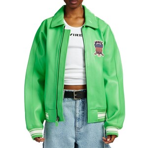 K&ouml;nnte beinhalten: Eine leuchtend gr&uuml;ne Bomberjacke aus lederartigem Material mit klassischem Kragen, Rei&szlig;verschluss vorne und gerippten B&uuml;ndchen mit wei&szlig;en Streifen. Auf der linken Brust befindet sich ein Aufn&auml;her mit US-Flaggenmotiv und dem Schriftzug AVIREX. Darunter wird ein wei&szlig;es Tanktop getragen.