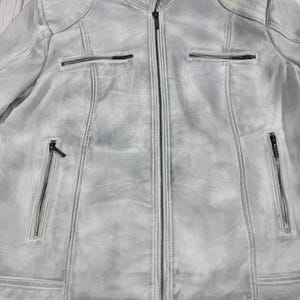 K&ouml;nnte beinhalten: Hellgraue Jacke mit durchgehendem Rei&szlig;verschluss und mehreren Rei&szlig;verschlusstaschen. Die Jacke hat ein abgenutztes, strukturiertes Aussehen mit gepolsterten Schulterdetails. Die Jacke hat eine neutrale Farbe und ist f&uuml;r verschiedene Outfits geeignet.