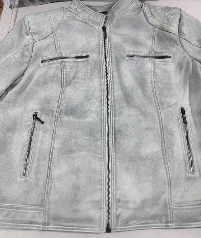 K&ouml;nnte beinhalten: Hellgraue Jacke mit durchgehendem Rei&szlig;verschluss und mehreren Rei&szlig;verschlusstaschen. Die Jacke hat ein abgenutztes, strukturiertes Aussehen mit gepolsterten Schulterdetails. Die Jacke hat eine neutrale Farbe und ist f&uuml;r verschiedene Outfits geeignet.