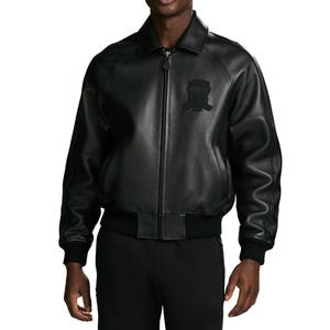 Puede incluir: Una chaqueta bomber de cuero negro con cuello cl&aacute;sico, cierre de cremallera frontal completo y pu&ntilde;os y dobladillo de punto acanalado. El pecho presenta un emblema bordado en negro tonal con un dise&ntilde;o de escudo y rayas horizontales.