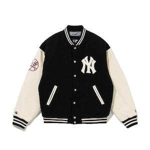 May include: Black and cream-colored varsity jacket featuring the New York Yankees logo. The jacket has a button-up front, white sleeves, and striped cuffs and hem. A Yankees logo patch is on the left sleeve.