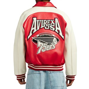 May include: A red and white leather varsity jacket featuring the text AVIREX USA, a football graphic, a winged profile illustration, and the text 75ers embroidered on the back. The jacket has a red collar, white sleeves, and red and white striped ribbed cuffs.