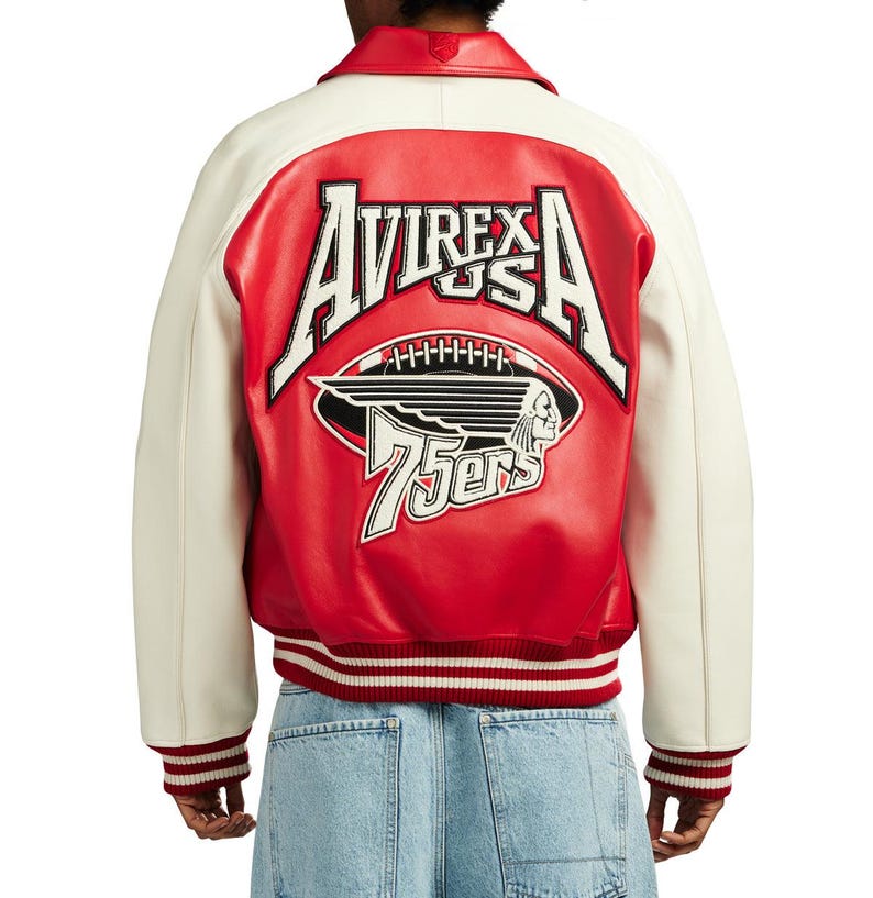 May include: A red and white leather varsity jacket featuring the text AVIREX USA, a football graphic, a winged profile illustration, and the text 75ers embroidered on the back. The jacket has a red collar, white sleeves, and red and white striped ribbed cuffs.