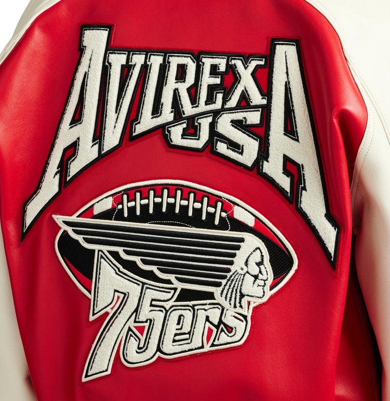 May include: A red and white varsity jacket featuring large white embroidered text that reads AVIREX USA. Below the text is a graphic of a football with wings and a profile of a person, accompanied by the white embroidered text 75ers.