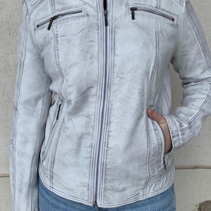 Könnte beinhalten: Hellgraue Jacke mit Reißverschluss und Used-Look. Die Jacke hat einen Stehkragen, mehrere Reißverschlusstaschen und gesteppte Schulterdetails. Das Model trägt eine blaue Jeans. Die Jacke ist eine stilvolle Oberbekleidung.