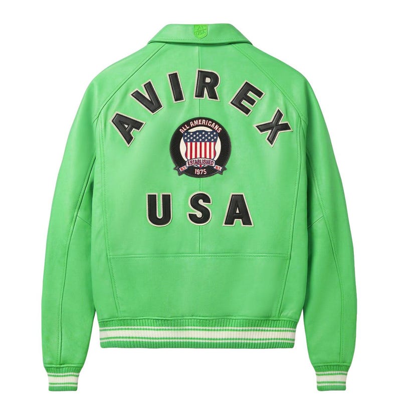 K&ouml;nnte beinhalten: Eine leuchtend hellgr&uuml;ne Lederjacke mit klassischem Kragen sowie gerippten B&uuml;ndchen und Saum mit wei&szlig;en Streifen. Auf der R&uuml;ckseite befinden sich der schwarze Schriftzug AVIREX und USA sowie ein rundes Abzeichen mit US-Flagge und dem Text ALL AMERICANS ESTABLISHED 1975.