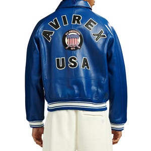 May include: A vibrant blue leather varsity jacket featuring the text AVIREX in large black letters across the upper back. Below the text is a circular patch with the American flag and the words ALL AMERICANS ESTABLISHED 1975. USA is printed in black below the patch.