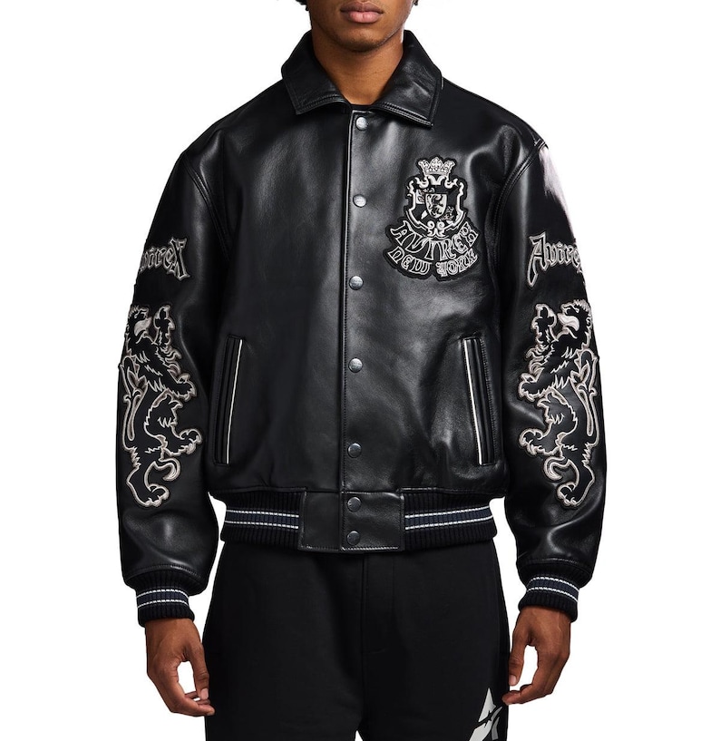 May include: A black leather varsity jacket featuring a pointed collar, snap-button front closure, and ribbed cuffs and hem with white stripes. The chest displays a crest patch with the text "AVIREX NEW YORK," while the sleeves feature lion embroidery.