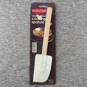 Peut inclure: Spatule de cuisine résistante à la chaleur Rubbermaid dans son emballage d'origine. La spatule a une tête en silicone blanche et un manche en bois clair. L'emballage présente le logo Rubbermaid et des informations sur le produit.