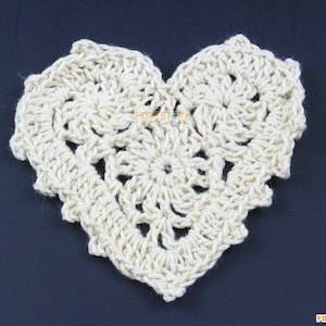 May include: A crocheted heart-shaped doily in a cream colour. The doily is made with a delicate stitch pattern and has a scalloped edge.